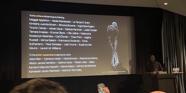 On the right, two skeletons in an intimate embrace, an image from X-Ray Portraits (2013) by Saiko Kanda and Mayuka Hayashi. On the left, a wall of text dedicated to writers and artist-researchers who inspired and influenced this talk. Writers: Maggie Appleton, Neda Atanasoski, La Tanya S. Autry, Kimberley Juanita Brown, Simone Browne, Ingrid Burrington, Tina M. Campt, Adrian Daub, Saidiya Hartman, Juliet Hooker, Tamara Kneese, Enuma Okoro, Olia Lialina, Katarszyna Nowaczyk-Basińska, Carl Öhman, Thao Phan, Legacy Russell, Minna Salami, Francesca Sobande, Tonia Sutherland, Tiera Tanksley, Julia Ticona, Suzanne Van Guens, Lauren M. Williams. Artist-Researchers: Jess Allen, Cameron Askin, Neta Bomani, Stephanie Dinkins, Allison Janae Hamilton, Sasha Huber, Vladen Joler, Saiko Kanda and Mayuka Hayashi, Merve Mepa, Mónica de Miranda, Kameelah Janan Rasheed, Alisha B. Wormsley.